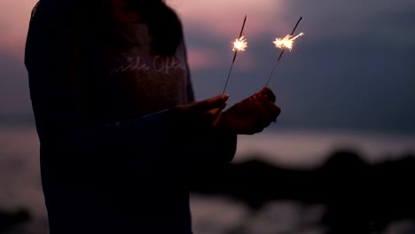 Young-asian-woman-stands-on-beach-with-sparkler-at-sunset-in-slow-motion.