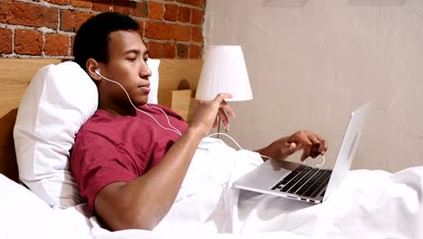 Afrikanischer-Mann-Musik-hören-am-Laptop-und-tanzen,-sitzen-auf-der-Treppe