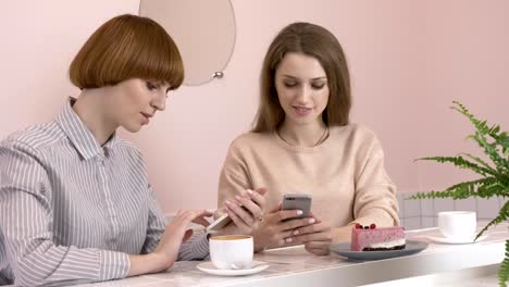 Two-young-Caucasian-girls-sitting-in-a-cafe-and-smiling,-using-a-smartphone,-texting,-typing.-The-girls-are-in-a-cafe.-60-fps