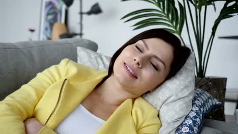 Lächelnde-junge-Frau-Blick-in-die-Kamera-während-der-Verlegung-auf-Sofa-zu-Hause