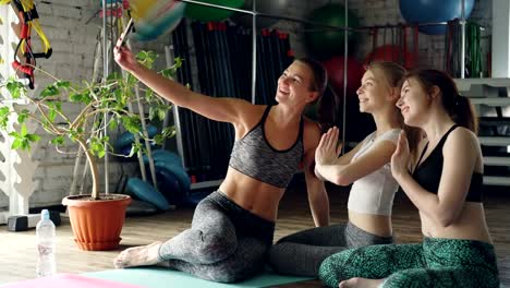 Pretty-girls-are-using-smartphone-to-take-selfie-in-yoga-studio.-Young-women-are-chatting,-posing-and-laughing,-they-are-having-fun-after-practice.