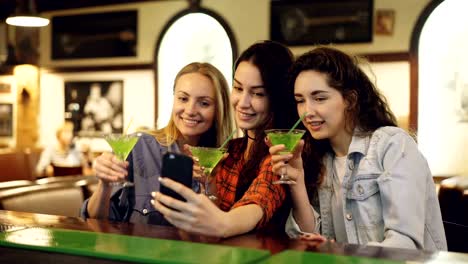 Las-mujeres-jóvenes-atractivas-toman-selfie-con-cócteles-en-la-barra.-Alegres-chicas-posando,-riendo-y-clanging-gafas.-Tomar-fotografías-para-el-concepto-de-cuenta-de-instagram.