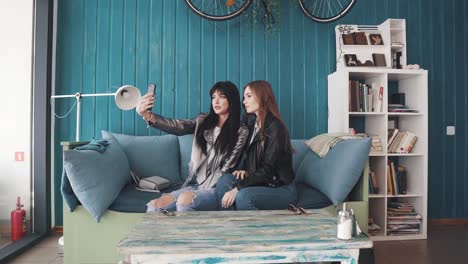 girlfriends-do-selfie-on-mobile-phone-cameras-while-sitting-in-a-cafe.-two-attractive-girls-take-pictures-on-the-camera-of-the-smartphone-and-fool-around