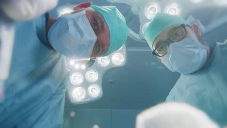 Low-Angle-Shot-POV-Patient-View:-Two-Professional-Surgeons-Holding-Surgical-Instruments-Starting-Surgery.