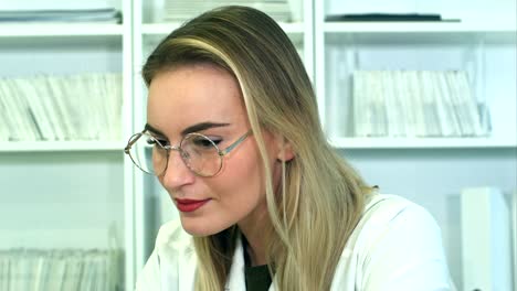 Attractive-young-female-doctor-in-glasses-sitting-at-desk-in-office