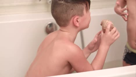 Two-little-boys-having-fun-with-seashell-while-taking-bath-in-bathtub