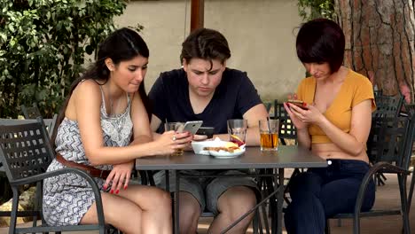 young-people,-smartphones---three-friends-at-the-cafe-focused-on-their-smartphones