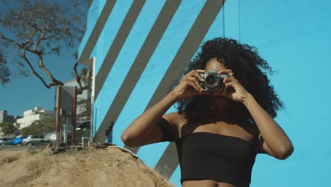 Schöne-junge-Frau-Fotografieren-mit-Film-Kamera-an-bunten-blauen-Wand