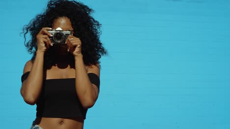 Beautiful-young-woman-shooting-photos-with-film-camera-against-colorful-blue-wall