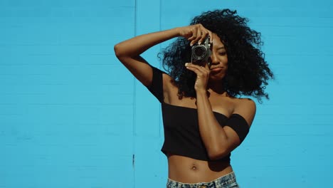 Beautiful-young-woman-shooting-photos-with-film-camera-against-colorful-blue-wall