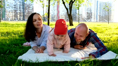 Padre-e-hija-están-mintiendo-con-la-madre-sobre-la-hierba-en-el-parque-en-verano.-Familia-feliz-con-el-bebé-descansando-en-el-parque-de-verano-al-atardecer