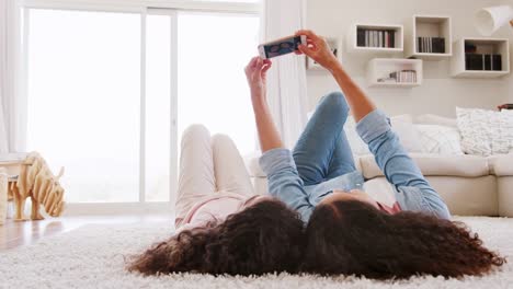 Mutter-und-Tochter-auf-Teppich-liegend-und-posieren-für-Selfie-zu-Hause