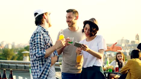 Pretty-young-woman-is-using-smartphone-to-take-selfie-with-her-cheerful-male-friends,-young-people-are-posing-then-laughing-and-watching-funny-photos.