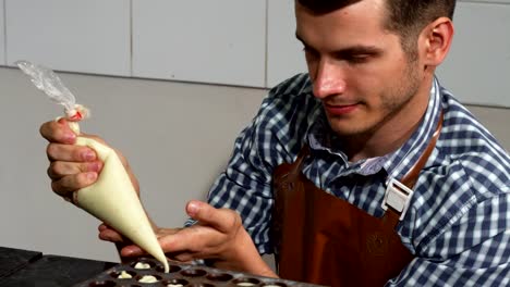 Young-male-confectioner-adding-vanilla-filling-into-chocolate-candy-molds