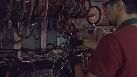 theme-small-business-bike-repair.-A-young-Caucasian-brunette-man-wearing-safety-goggles,-gloves-and-an-apron-uses-a-hand-tool-to-repair-and-adjust-the-bike-in-the-workshop-garage