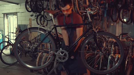 theme-small-business-bike-repair.-A-young-Caucasian-brunette-man-wearing-safety-goggles,-gloves-and-an-apron-uses-a-hand-tool-to-repair-and-adjust-the-bike-in-the-workshop-garage