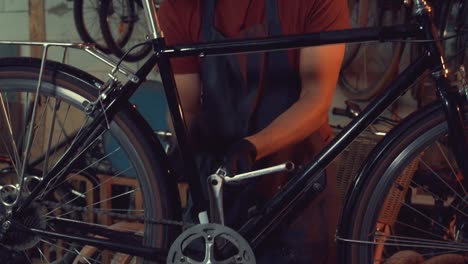 theme-small-business-bike-repair.-A-young-Caucasian-brunette-man-wearing-safety-goggles,-gloves-and-an-apron-uses-a-hand-tool-to-repair-and-adjust-the-bike-in-the-workshop-garage