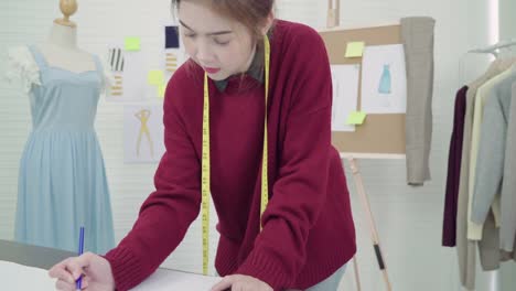 Young-Asian-woman-fashion-designer-drawing-using-pencil-and-looking-at-paper-while-working-in-the-workshop-studio.