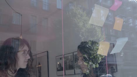 Two-businesswomen-brainstorm-on-windows-wall-over-real-estate