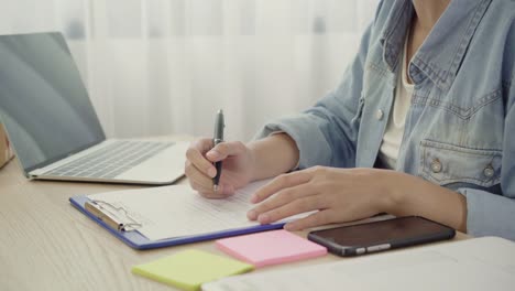 Beautiful-smart-Asian-young-entrepreneur-business-woman-owner-of-SME-checking-product-on-stock-and-write-on-clipboard-working-at-home.-Small-business-owner-at-home-office-concept.