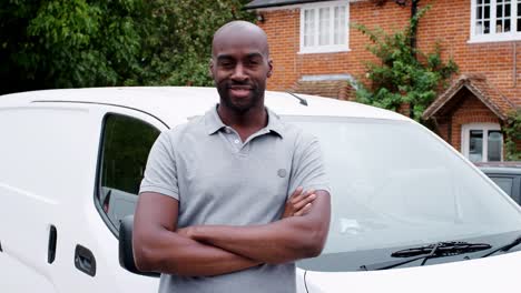 Young-adult-black-tradesman-standing-and-leaning-on-his-white-van-smiling-to-camera-crosses-his-arms,-close-up