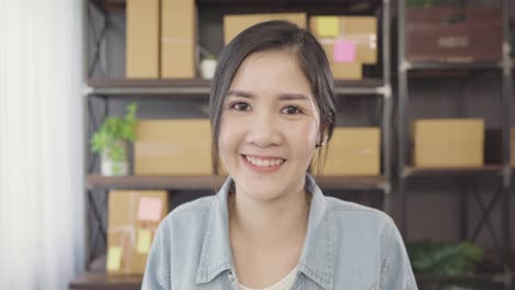 Business-woman-feeling-happy-smiling-and-looking-to-camera-while-working-in-her-office-at-home.-Beautiful-Asian-young-entrepreneur-owner-of-SME-with-small-business-owner-at-home-office-concept.