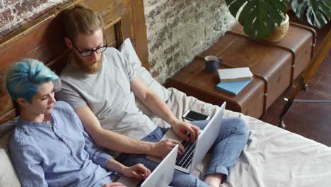 Pareja-hipster-con-computadoras-portátiles-trabajando-de-cama