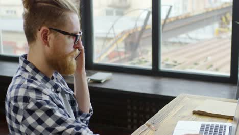 Hipster-Man-Talking-on-Phone-and-Working-on-Laptop