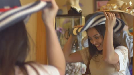 Dos-mujeres-jóvenes-tratando-en-sombreros-en-una-tienda-y-mirando-en-un-espejo