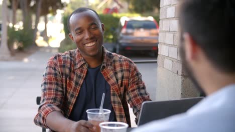 Two-happy-male-friends-with-cold-drinks-outside-coffee-shop