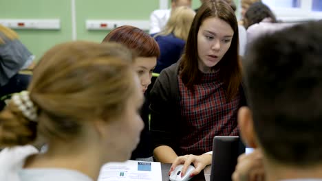 Close-up-of-business-team-preparing-the-presentation-of-their-startup.-Young-brown-haired-girl-in-plaid-dress-is-explaining-some-information-to-her-collegues