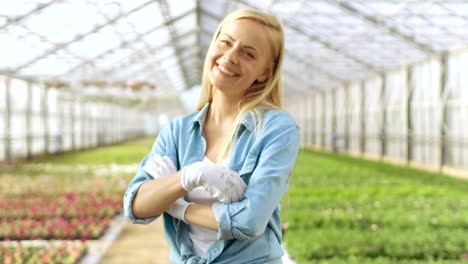 An-einem-sonnigen-Tag-schöne-Blonde-Gärtner-steht-lächelnd-in-ein-Gewächshaus-voller-bunter-Blumen.