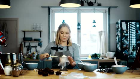 Young-beautiful-woman-standing-on-the-kitchen-and-cooking-cupcakes.-Blonde-female-puts-the-cream-in-pastry-bag