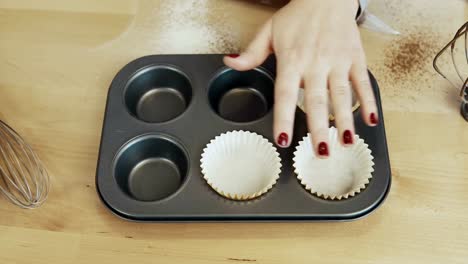 Vista-de-primer-plano-de-mano-mujer-poniendo-las-tazas-de-papel-en-la-bandeja-para-hornear.-Mujer-cocina-cupcakes.-Lapso-de-tiempo