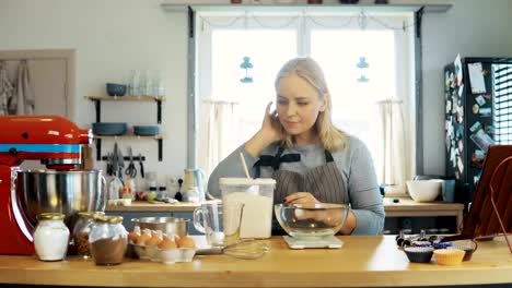 Junge-blonde-Frau-mit-der-Küche-Waagen-wiegen-das-Mehl.-Schöne-weibliche-Backen-Muffins-auf-dem-Küchentisch