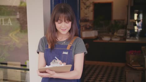 Beautiful-Young-Deli-Owner-Writing-In-Clipboard-Outside-Store