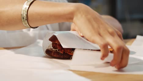 Woman-wrapping-sandwich-for-take-away-at-a-deli,cafe,-mid-section