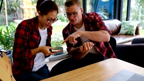 Inicio-pequeño-empresario-hablando-en-el-lugar-de-trabajo.-vendedor-freelance-cheque-orden-de-producto-con-smartphone-en-la-tienda.-Joven-pareja-mira-el-teléfono-móvil.-Online-venta,-comercio-electrónico,-envío-concepto