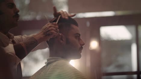 Young-stylish-barber-with-tattoos-cutting-and-styling-man's-hair