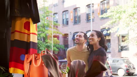 Smiling-couple-looking-at-clothes-in-a-shop-window