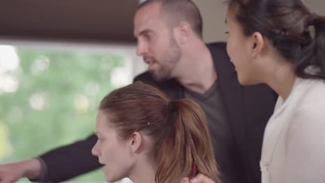 Close-up-of-colleages-gathered-around-a-computer-in-a-bright-office-and-reading-charts