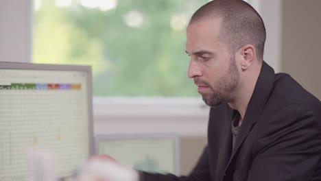 Close-up-of-a-business-man-in-a-bright-office-entering-data-into-a-computer-and-jotting-notes