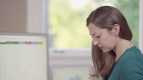 Close-up-of-a-business-woman-in-a-bright-office-entering-data-into-a-computer-and-jotting-notes