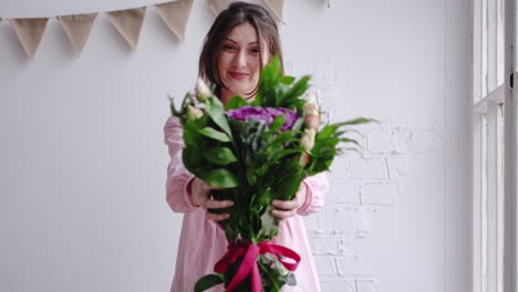 Florist-girl-looks-at-the-camera-and-shows-the-bouquet.-Portrait-in-a-flower-shop