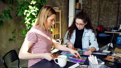 Female-designers-are-working-with-color-palettes-to-determine-colors-on-photograph.-They-are-celebrating-success-with-high-five.-Work-day-in-design-company-concept.