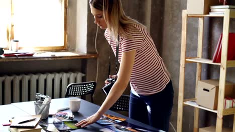 Young-female-photographer-is-making-flat-lay-from-colorful-photos-on-table-and-shooting-them-with-camera.-She-is-displaying-pictures-near-color-palette-and-markers-on-desk.