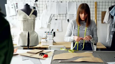 Young-pretty-seamstress-is-measuring-clothing-patterns-with-tape-measure-in-her-modern-tailor's-shop.-Getting-ready-for-sewing-clothes-concept.