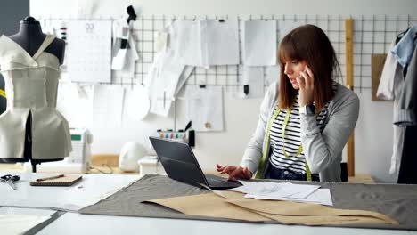 Designer-Kleidung-ist-diskutieren-Kleidungsstück-Skizzen-auf-Handy-und-Laptop-eingeben-der-Informationen.-Anstrengenden-Tag-in-Kleidung-entwerfen-Studio-Konzept.