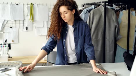 Sastre-mujer-está-lanzando-perno-de-la-tela-en-mesa-de-estudio-tomando-el-dibujo-de-prendas-de-vestir-y-dibujo-sobre-papel.-Diseño-de-ropa-y-elegir-concepto-textil.