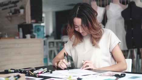 young-fashion-designer-girl-makes-a-sketch-in-pencil-at-the-atelier.-business-woman-with-Asian-appearance-working-in-the-office